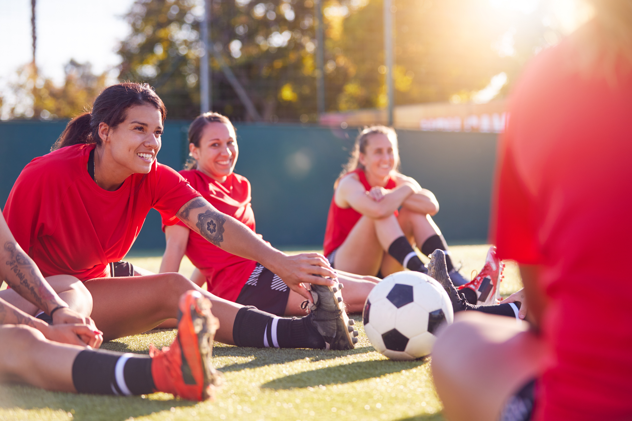 Womens Football Team Stretching Whilst Training For Soccer Match On Outdoor Astro Turf Pitch