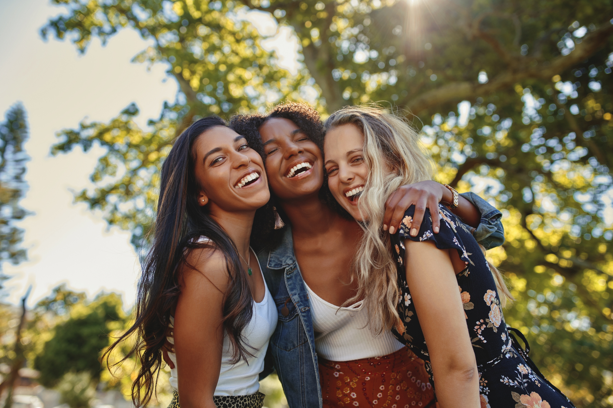 Cheerful excited positive modern group of female friends hugging together in park and laughing and having fun