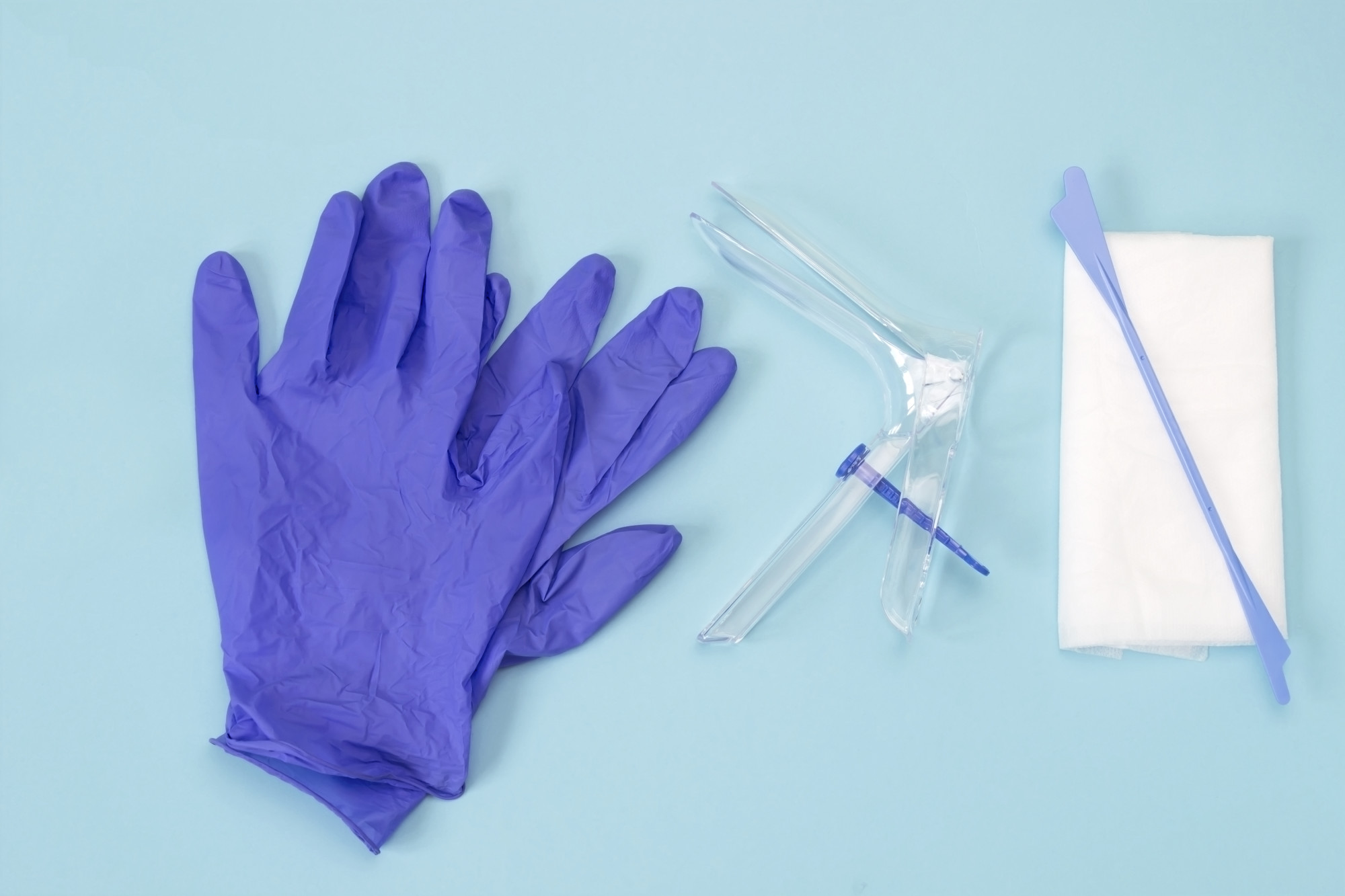 An overhead photo of the vaginal speculum, white napkin, medicine gloves and spatula. Medical plastic tool for holding open the vagina during medical investigation. Feminine woman health diagnosis